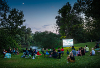 Familier ser en film under åben himmel ved floden i aftensolen i ferieparken Huttopia La Plage Blanche.