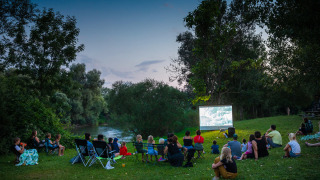 Familias disfrutan de una película al aire libre junto al río al atardecer en Huttopia La Plage Blanche, Francia.