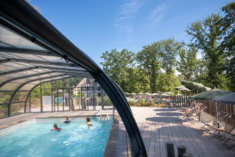Piscina cubierta y terraza con tumbonas en Huttopia Wattwiller, rodeada de árboles en Grand Est, Francia.