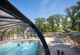 Piscine couverte et terrasse en bois au Huttopia Wattwiller, entourées d’arbres dans le Grand Est, France.
