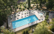 Luftfoto af swimmingpool og solstole omgivet af træer på Huttopia Wattwiller feriepark i Grand Est, Frankrig.