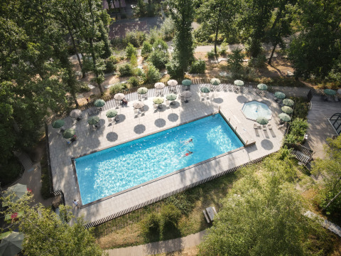 Luftfoto af swimmingpool og solstole omgivet af træer på Huttopia Wattwiller feriepark i Grand Est, Frankrig.