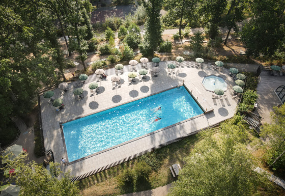 Vista aérea de una piscina y tumbonas con sombrillas en Huttopia Wattwiller, parque vacacional en Grand Est, Francia.