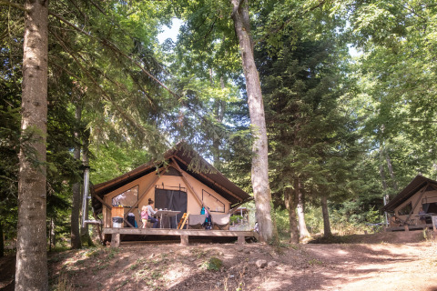 Familias disfrutan del aire libre en terrazas de cabañas de Huttopia Wattwiller en Grand Est, Francia.