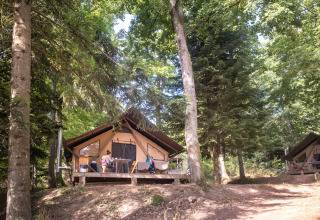 Familles profitent des terrasses en bois de lodges sous les arbres à Huttopia Wattwiller, Grand Est, France.