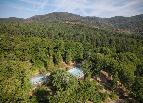 Vista aérea del parque vacacional Huttopia Wattwiller en Grand Est, Francia, rodeado de bosque y montañas.