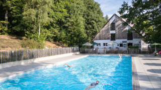 Outdoor swimming pool at Huttopia Wattwiller holiday park, nestled by trees and patio umbrellas in France.