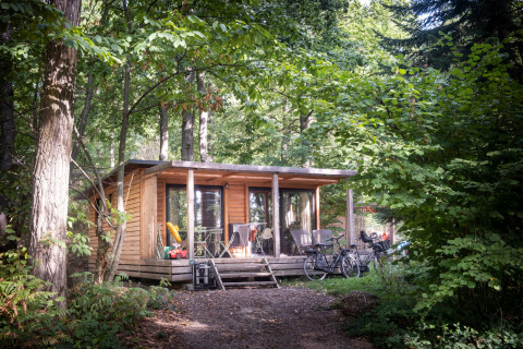 Houten hut in Huttopia Wattwiller, Grand Est, Frankrijk, met fietsen en terras tussen het groen.