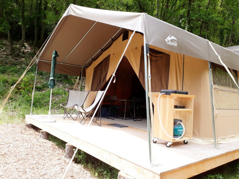 Safari tent Sweet op houten vlonder in het bos, met stoelen en kampeeruitrusting onder de luifel.