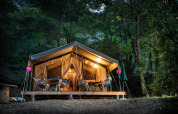 Tienda safari Tent Sweet en Huttopia Gorges du Tarn, Francia, iluminada y rodeada de un bosque verde.