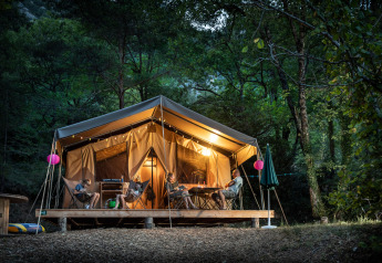 Safari tent Tent Sweet at Huttopia Gorges du Tarn in France, warmly lit and nestled among tall forest trees.