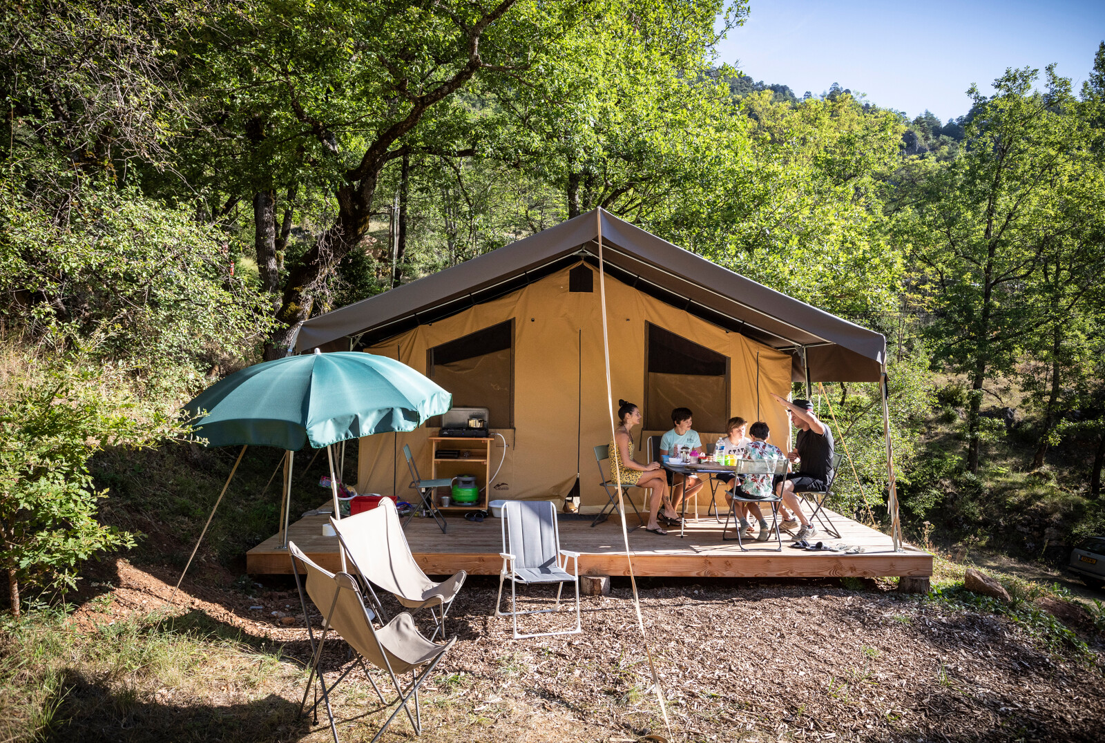 Gezin geniet van een maaltijd buiten in safari tent Tent Sweet bij Huttopia Gorges du Tarn, Frankrijk.
