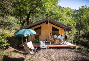 Familie isst zusammen auf der Terrasse eines Safari-Zelts Tent Sweet bei Huttopia Gorges du Tarn, Frankreich.