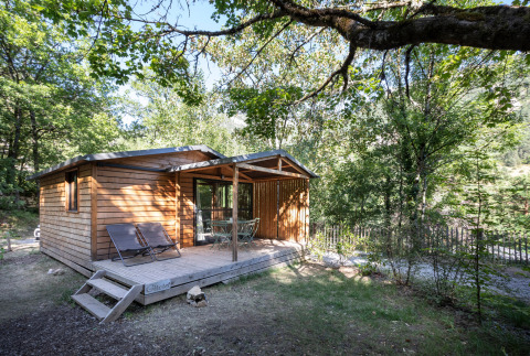 Houten vakantiestudio Chalet Evasion met terras, stoelen en loungestoelen te midden van zomerse bossen.