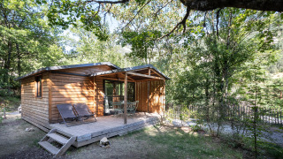 Cabaña de madera llamada Chalet Evasion con terraza y tumbonas, rodeada de naturaleza y árboles en verano.