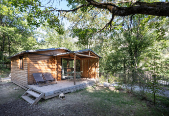 Houten chalet genaamd Chalet Evasion met veranda en stoelen, omringd door zomerse bosrijke natuur.