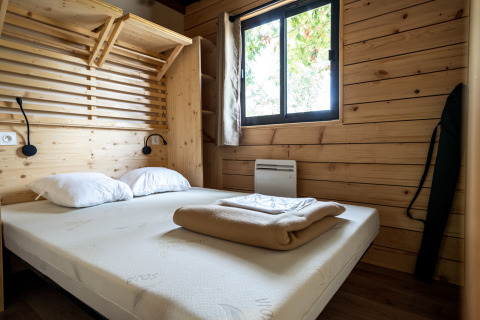 Schlafzimmer im Chalet Evasion Glamping mit Holzwänden, Doppelbett, weißen Kissen und Fenster.