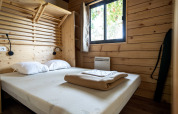 Bedroom at Chalet Evasion glamping with wooden walls, double bed, white pillows, window and shelves.