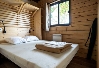 Schlafzimmer im Chalet Evasion Glamping mit Holzwänden, Doppelbett, weißen Kissen und Fenster.