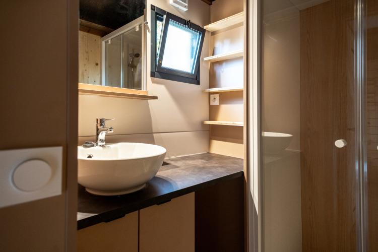 Baño moderno en Chalet Evasion, Huttopia Gorges du Tarn, con lavabo, estantes, ventana y ducha acristalada.
