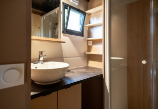 Baño moderno en Chalet Evasion, Huttopia Gorges du Tarn, con lavabo, estantes, ventana y ducha acristalada.