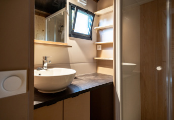 Baño moderno en Chalet Evasion, Huttopia Gorges du Tarn, con lavabo, estantes, ventana y ducha acristalada.