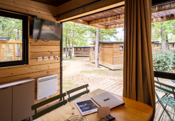 Blick aus der Chalet Evasion Glamping-Unterkunft mit Terrasse, Holztisch und anderen Chalets draußen.