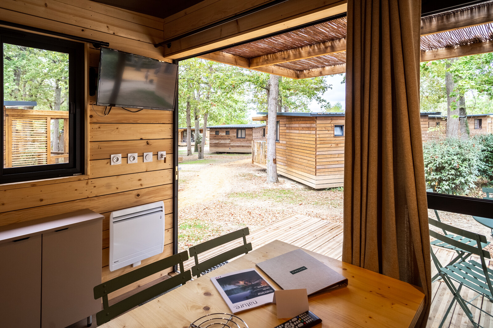 Uitzicht vanuit het Chalet Evasion glampingverblijf met houten terras, buitenzitje en andere chalets.