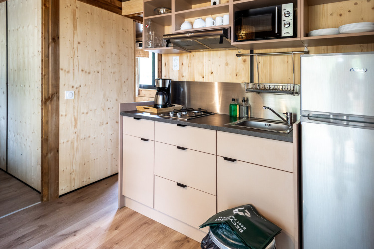 Moderne Küchenzeile im Chalet Evasion Glamping mit Herd, Spüle, Kaffeemaschine und Kühlschrank.