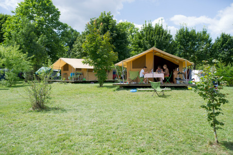 Safari-Bungalowzelt Classic im Huttopia La Plage Blanche, Frankreich, umgeben von grüner Natur.