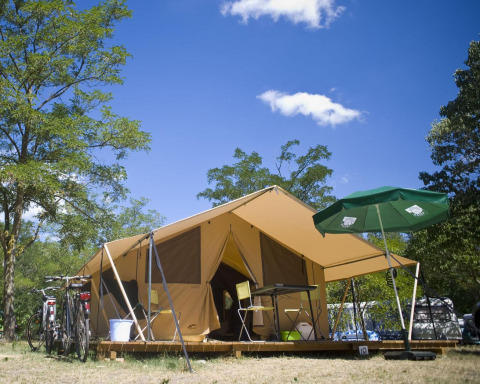 Tienda safari Bungalow Tent Classic con bicicletas, sombrilla y muebles de camping bajo un cielo azul.