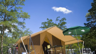 Safari telt Bungalow Tent Classic med cykler, paraply og campingmøbler under en blå himmel med skyer.