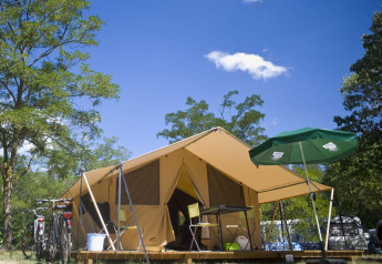 Safari-Zelt Bungalow Tent Classic mit Fahrrädern, Campingmöbeln und Sonnenschirm unter blauem Himmel.