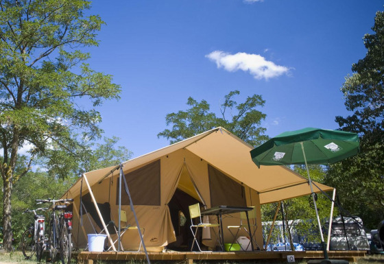 Safari tent Bungalow Tent Classic met fietsen, parasol en kampeerinrichting onder een blauwe lucht.