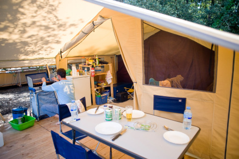 Interieur van een safaritent met eettafel, keukenhoek en een persoon die aan het koken is.