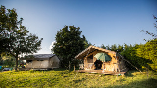 Toile&Bois tent Sweet safari tent on grassy site with trees, wooden deck, and umbrella in sunlight.