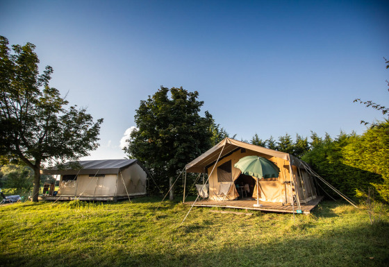 Toile&Bois tent Sweet safaritent op een groene weide met bomen, houten terras en parasol erbij.