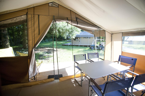 Vista interior de una safari tent Toile&Bois tent Sweet con mesa, sillas y entrada abierta hacia la naturaleza.