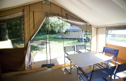 Vista interior de una safari tent Toile&Bois tent Sweet con mesa, sillas y entrada abierta hacia la naturaleza.