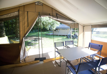 Vista interior de una safari tent Toile&Bois tent Sweet con mesa, sillas y entrada abierta hacia la naturaleza.
