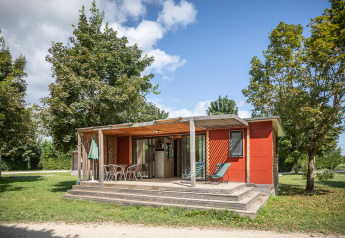 Casa móvil Vancouver con terraza de madera, sillas y mucho verde, rodeada de árboles y cielo soleado.