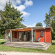 Mobile home Vancouver-lodge med træterrasse, havemøbler og grønne omgivelser under blå himmel.