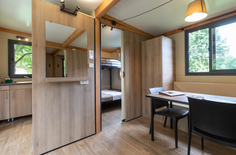 Interior de la Mobile home Vancouver en Huttopia La Plage Blanche, Francia, con mesa comedor y literas.