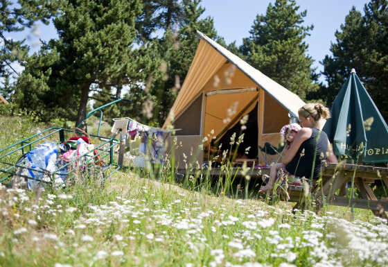 En familie sidder foran et Canadienne-safaritelt i naturen, omgivet af vilde blomster og træer.