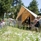En familie sidder foran et Canadienne-safaritelt i naturen, omgivet af vilde blomster og træer.