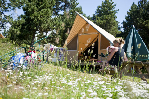 Family enjoying time outside a Canadienne safari tent in nature, surrounded by wildflowers and trees.