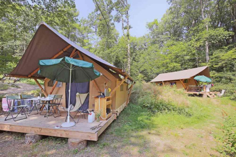 Canadienne Safari-Zelte bei Huttopia Wattwiller in Frankreich, mit Holzterrasse, Sonnenschirm und Wald.