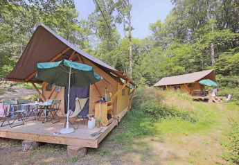 Tentes safari Canadienne à Huttopia Wattwiller en France, avec terrasse en bois, parasols et forêt verdoyante.