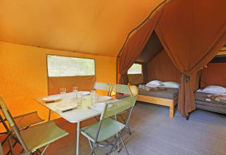Innenraum eines Canadienne Safari-Zeltes im Huttopia Wattwiller, Frankreich, mit Essbereich und Betten.