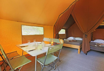 Interior de una tienda canadienne en Huttopia Wattwiller, Francia, con área de comedor y camas visibles.